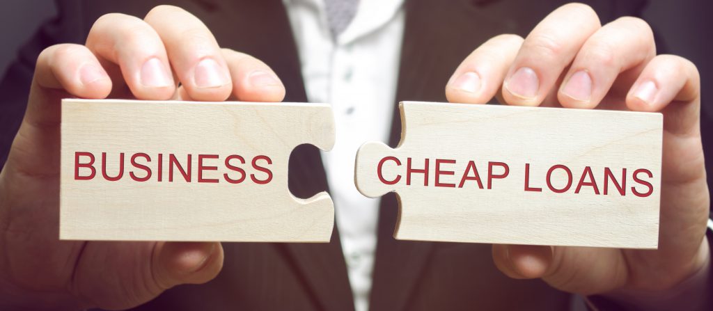 Businessman collects wooden puzzles with the words Business and cheap loans. Cheap and affordable loans to support small and medium businesses. Marshall plan. Stimulate economic growth.