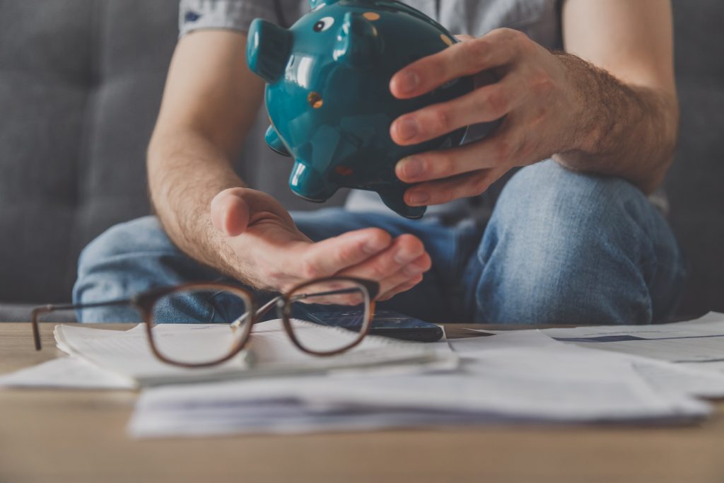 Man sitting at a table full of unpaid bills shakes out the last penny from the piggy bank. Spend your last savings. Unemployment, poverty, bankruptcy concept.