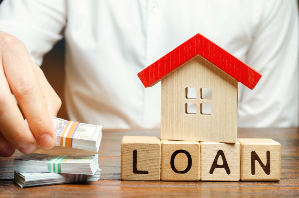 Wooden blocks with the word Loan, house and money in the hands of a businessman. The concept of buying an apartment or house in debt. Mortgage credit lending. Payment of interest rates. Saving money